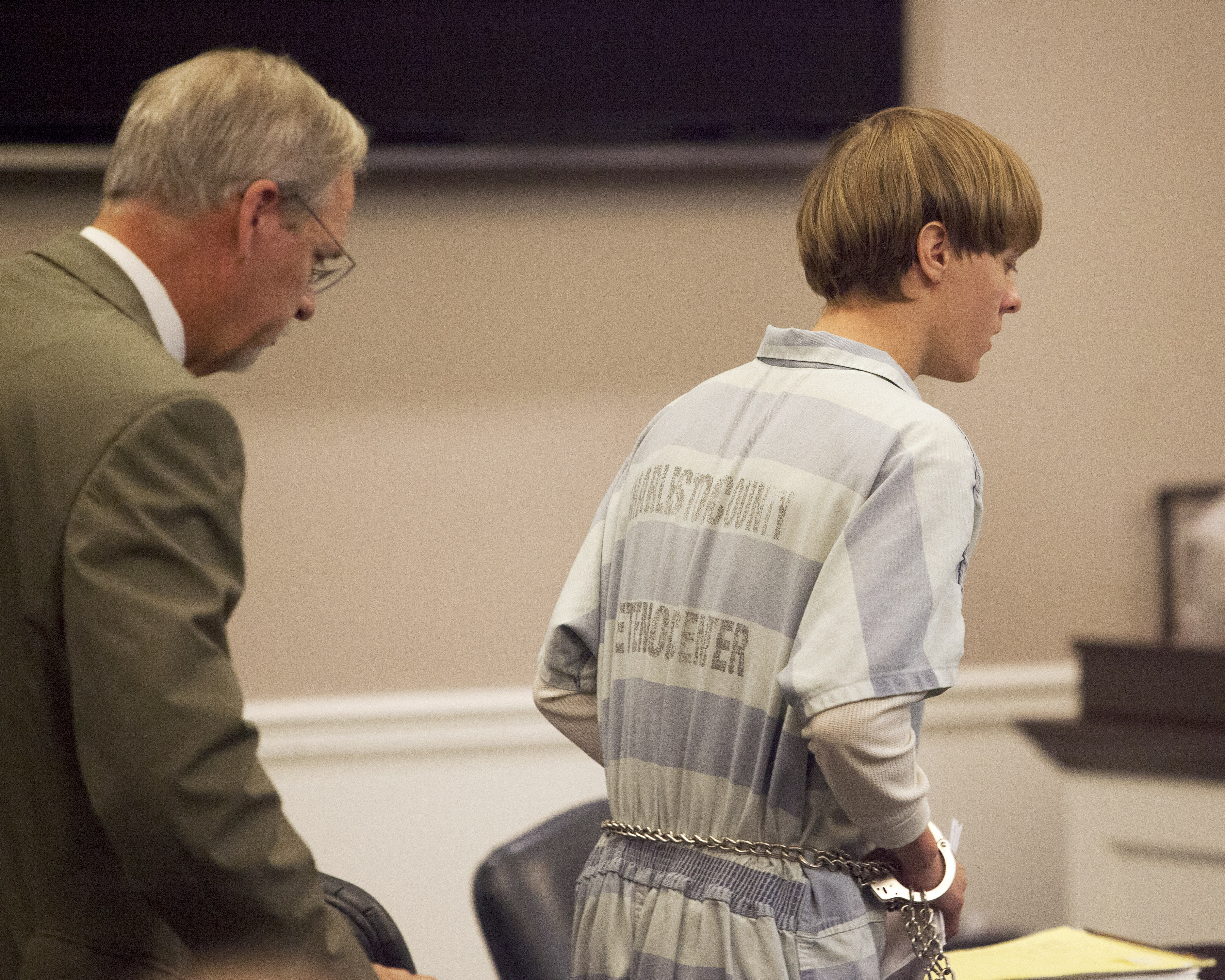 Dylann Roof (R), the 21-year-old man charged with murdering nine worshippers at a historic black church in Charleston last month, is helped to his chair by chief public defender Ashley Pennington during a hearing at the Judicial Center in Charleston