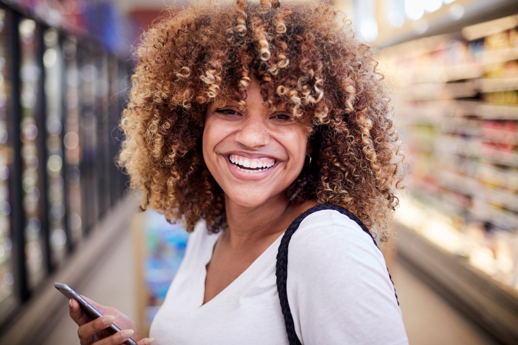 Black woman holding cell phone smiling in grocery store